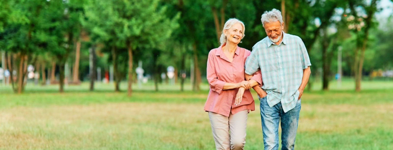 elderly man and woman walking in grass with arms linked